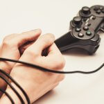 video game addiction represented by controller wire wrapped around young man's wrists