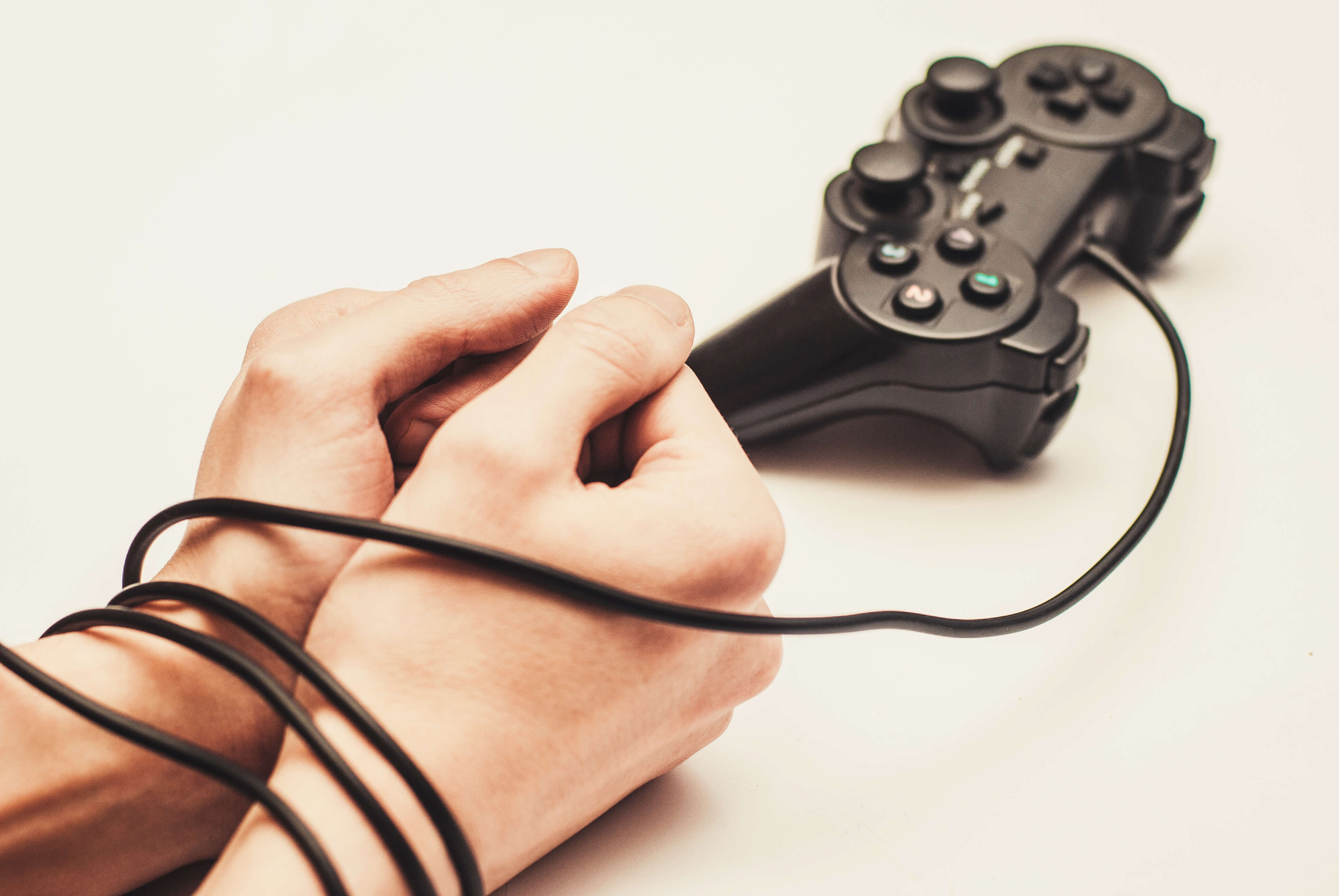 video game addiction represented by controller wire wrapped around young man's wrists